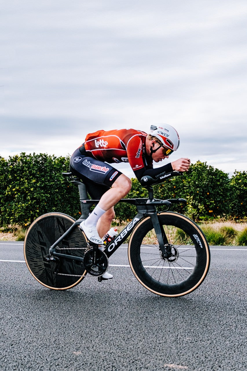 Cyclist wearing DeFeet cycling socks in a time trial position on a road bike with aero wheels.