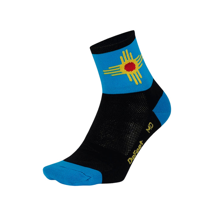 Aireator 3" New Mexico is a black sock with a bright blue cuff featuring the flag's graphic sun symbol in yellow with a red center