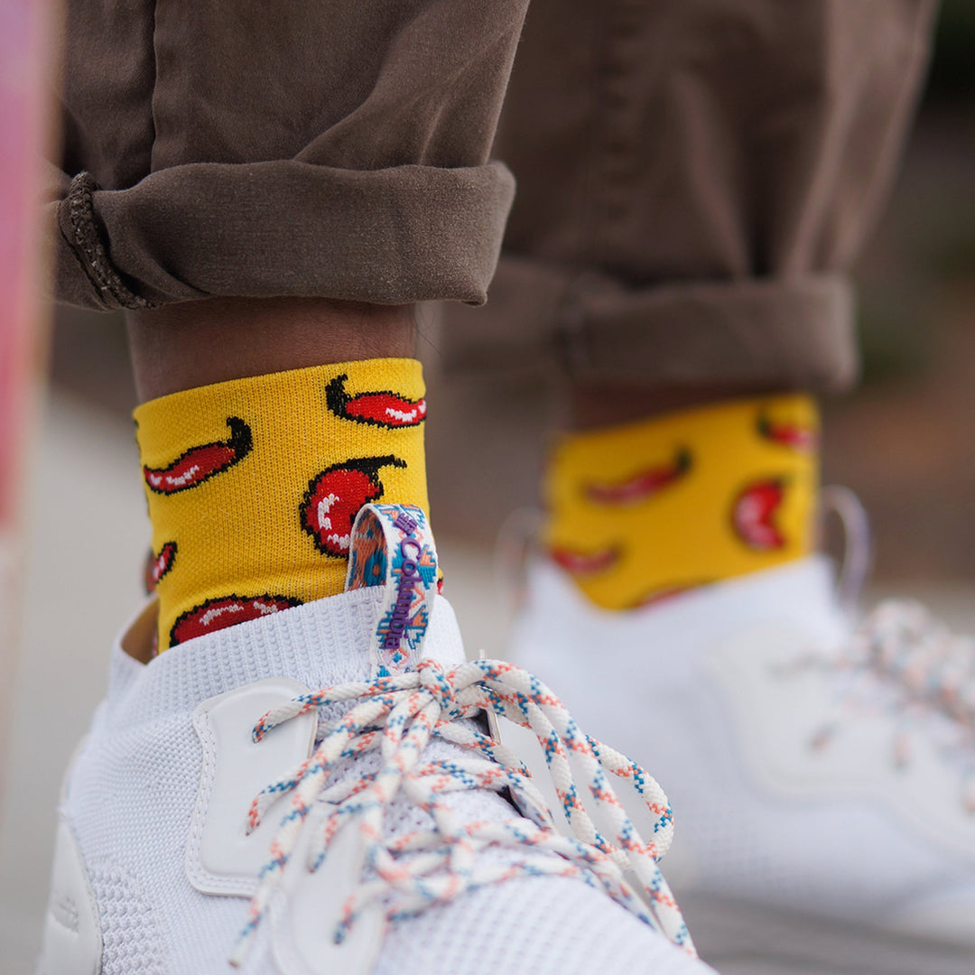 a man wearing white tennis shoes with yellow 3" DeFeet Aireator cycling socks in yellow with red chili peppers