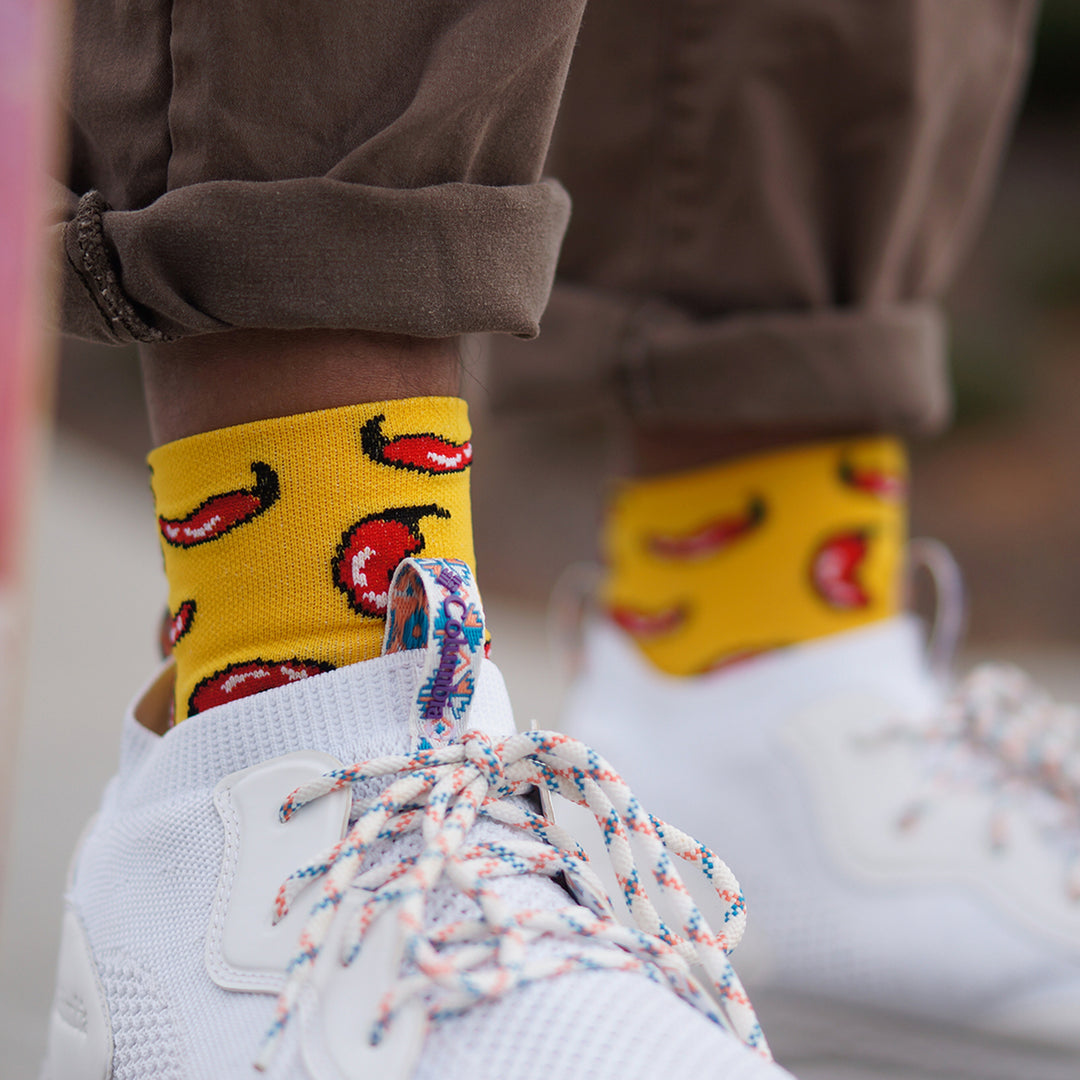 a man wearing white tennis shoes with yellow 3" DeFeet Aireator cycling socks in yellow with red chili peppers